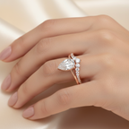 Rose gold ring with a pear-shaped diamond on a hand against a beige background